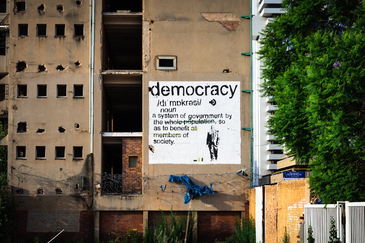 An abandoned building features a prominent democracy poster amidst urban decay.